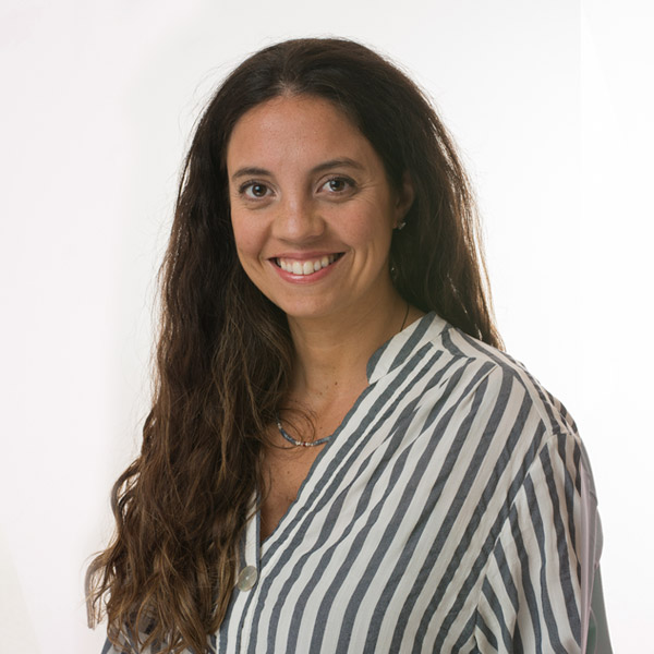 Mujer de pelo ondulado y largo, castaño y ojos marrones sonriendo. Viste blusa a rayas.